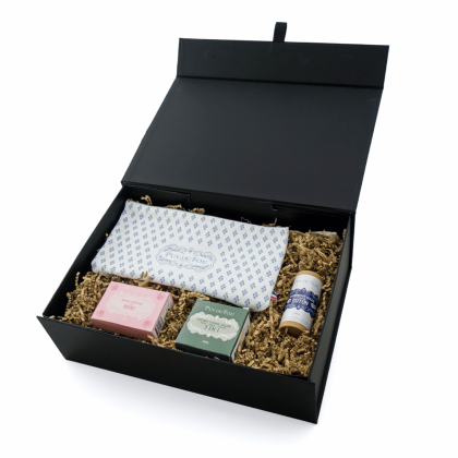Coffret bien-être vu en perspective, avec les produits disposés à l’intérieur : pochette, savon végétal, lavant solide et déodorant fleur de coton.