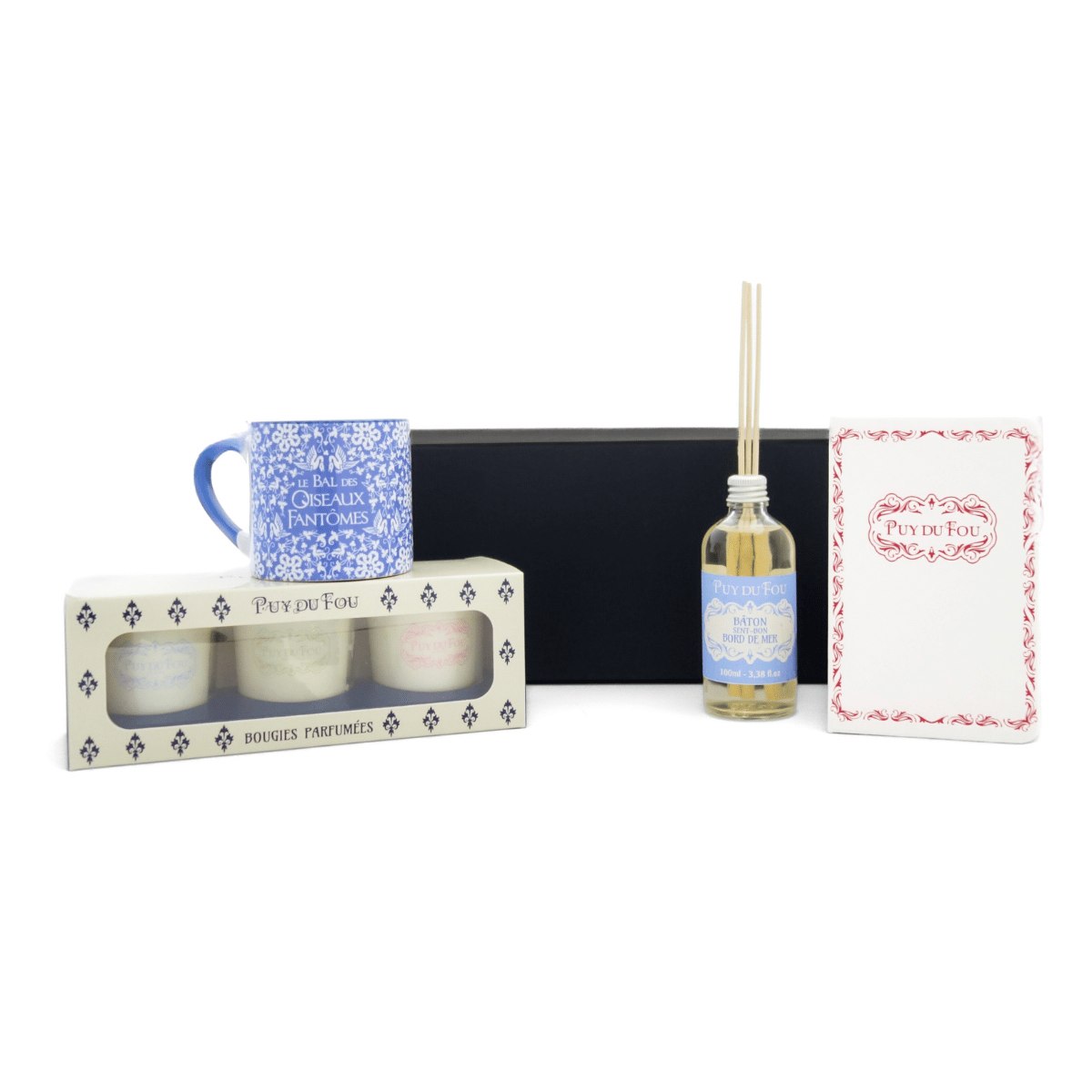 Produits du coffret Maison & Senteurs alignés devant la boîte : bougies parfumées, mini mug bleu, carnet A6 Puy du Fou et diffuseur de parfum.