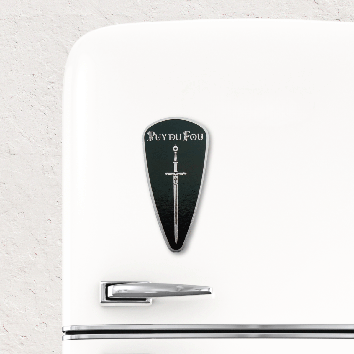 Magnet bouclier Exkalibur noir fixé sur réfrigérateur blanc vintage montrant son usage décoratif et pratique