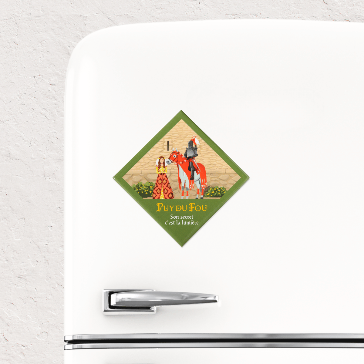 Magnet souvenir Puy du Fou Le Secret de la Lance collé sur un réfrigérateur blanc, illustration de Marguerite et du chevalier Fulgent en armure